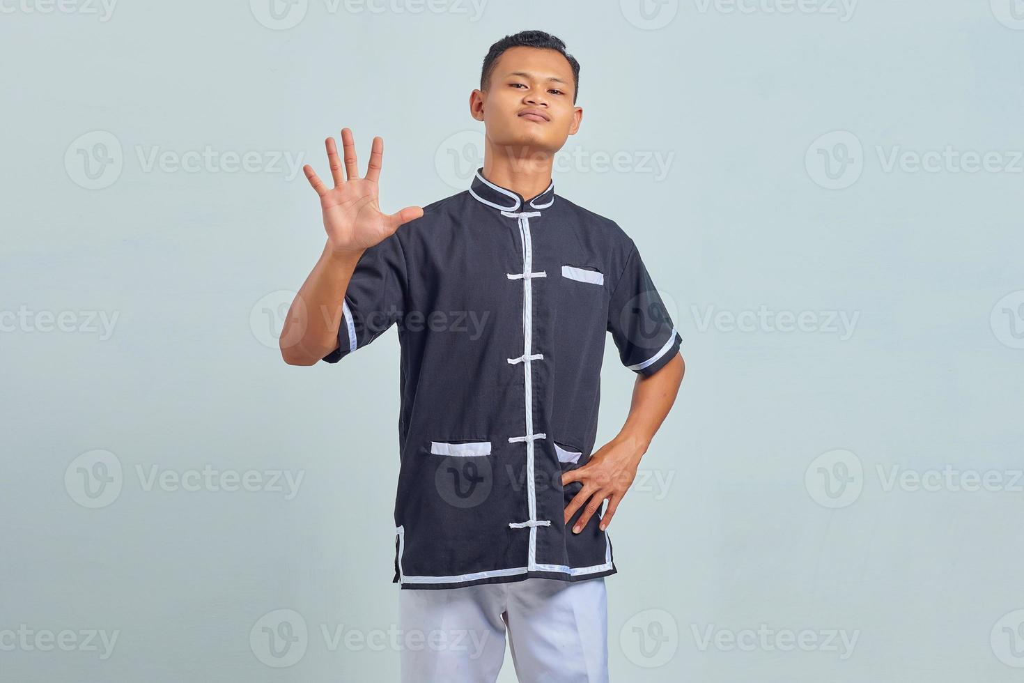 Portrait of Asian young man wearing karate making number five sign with finger over gray background photo