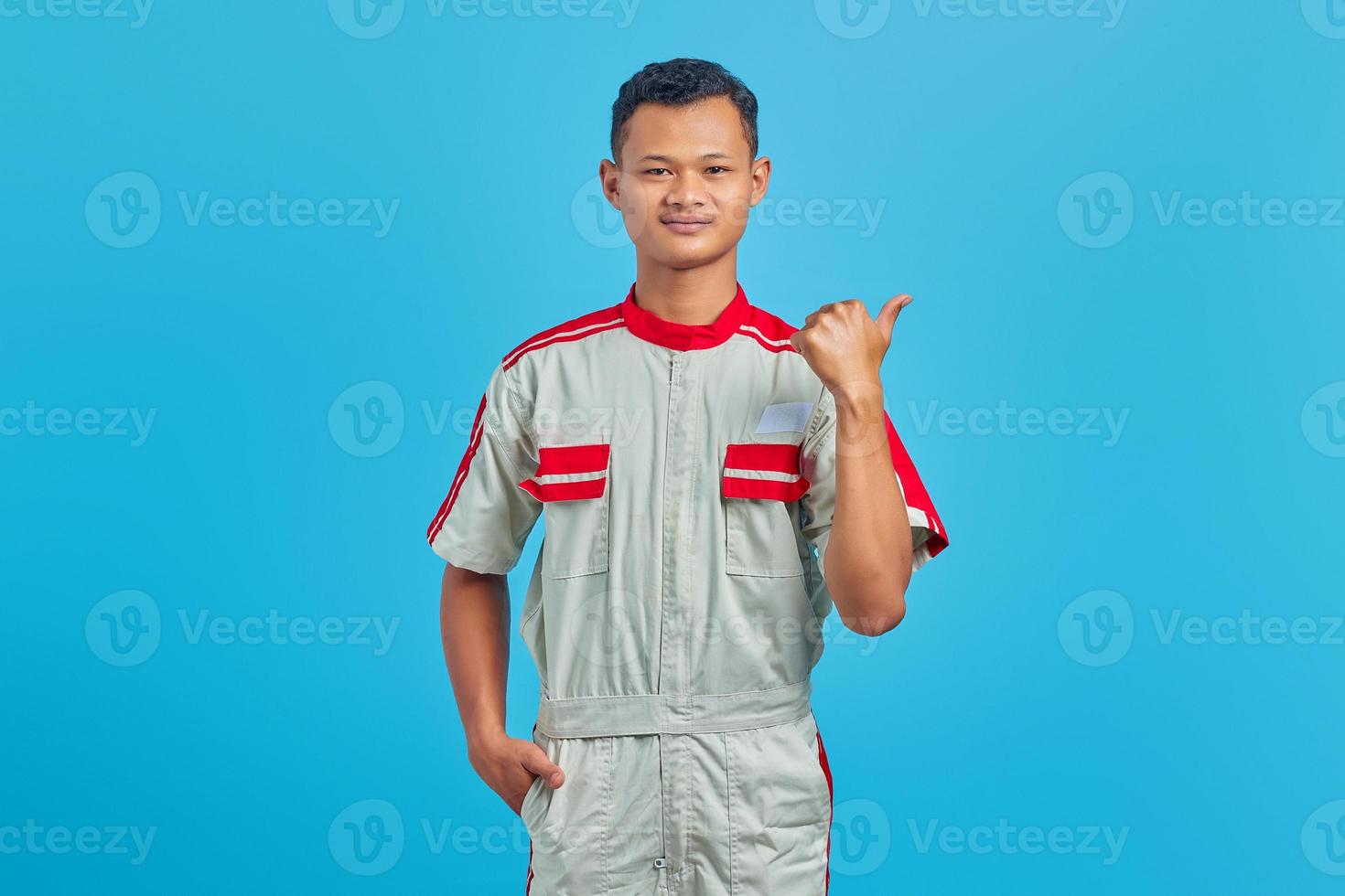 Retrato de feliz joven mecánico con el dedo acusador en el espacio de la copia sobre fondo azul. foto