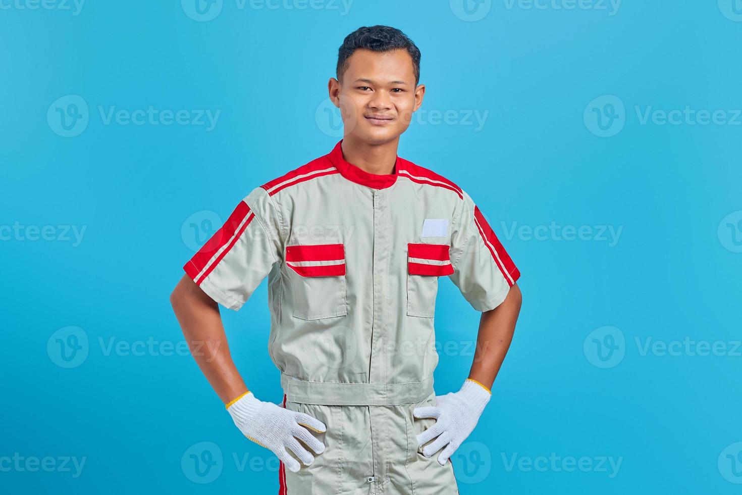 Portrait of smiling young Asian mechanic holding hands confidently over blue background photo