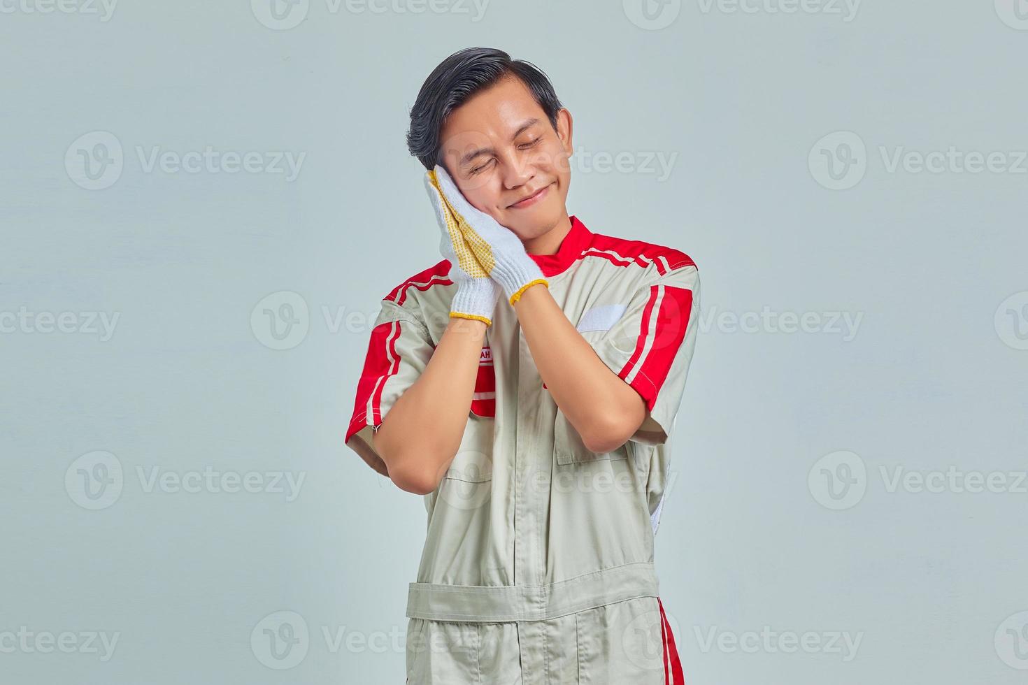 Portrait of cheerful handsome man wearing mechanical uniform with sleeping gesture on gray background photo