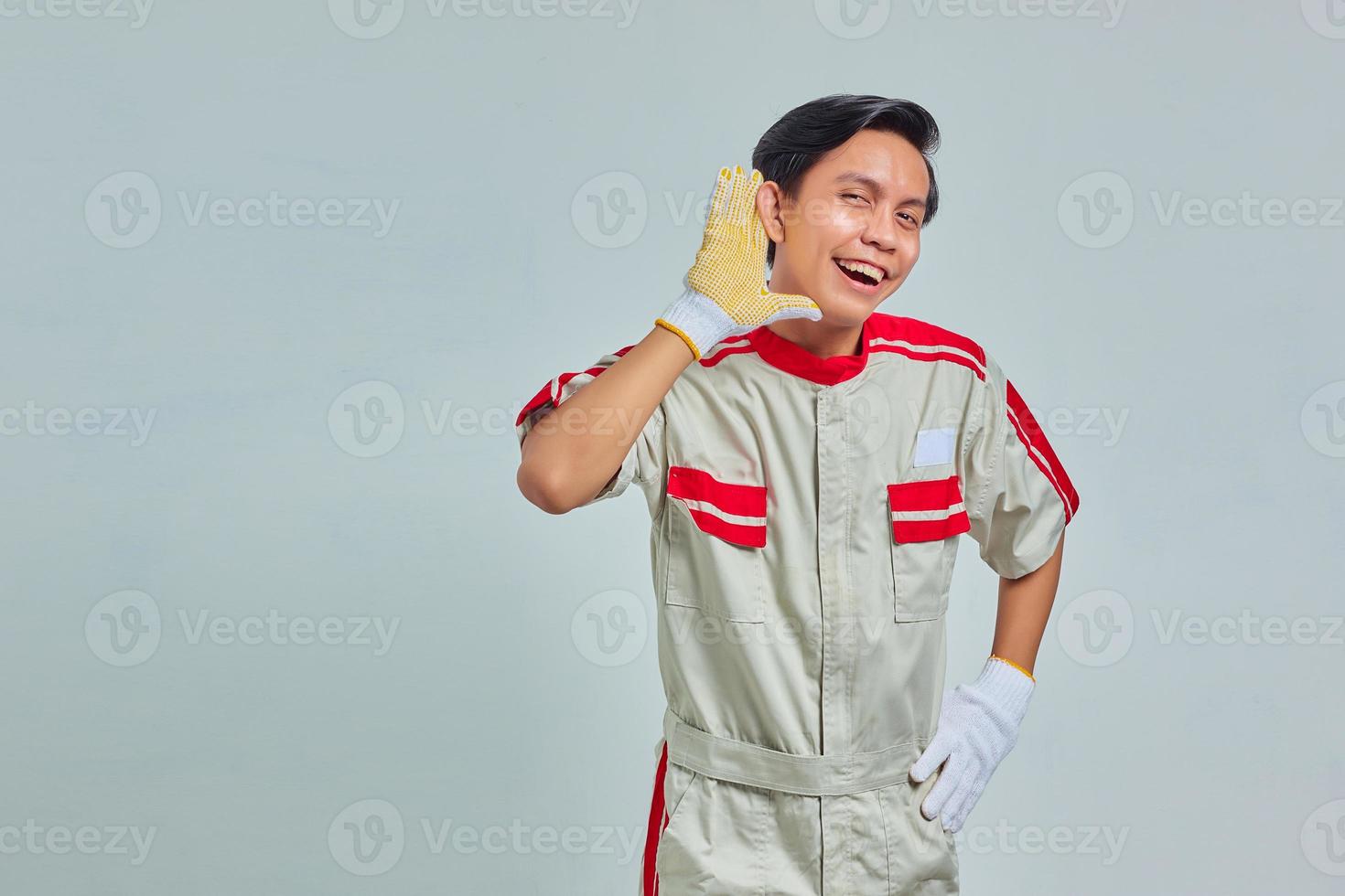 Retrato de hombre guapo serio vestido con uniforme mecánico tratando de escuchar una conversación secreta sobre fondo gris foto