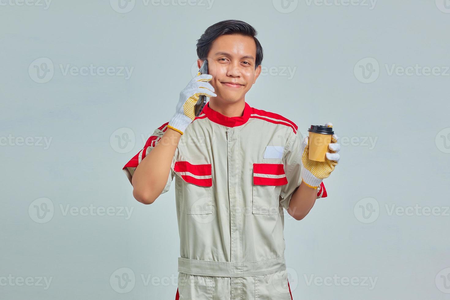 Happines young mechanic talking on smartphone and holding coffee on gray background photo