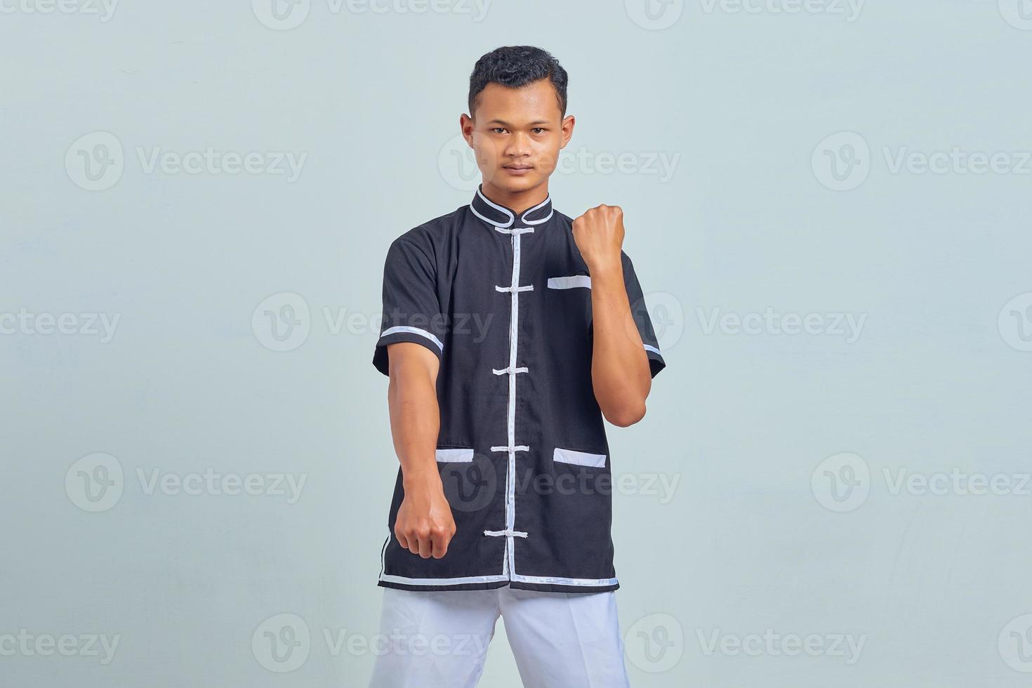 Portrait of handsome asian sportsman wearing kimono practicing karate isolated over gray background photo