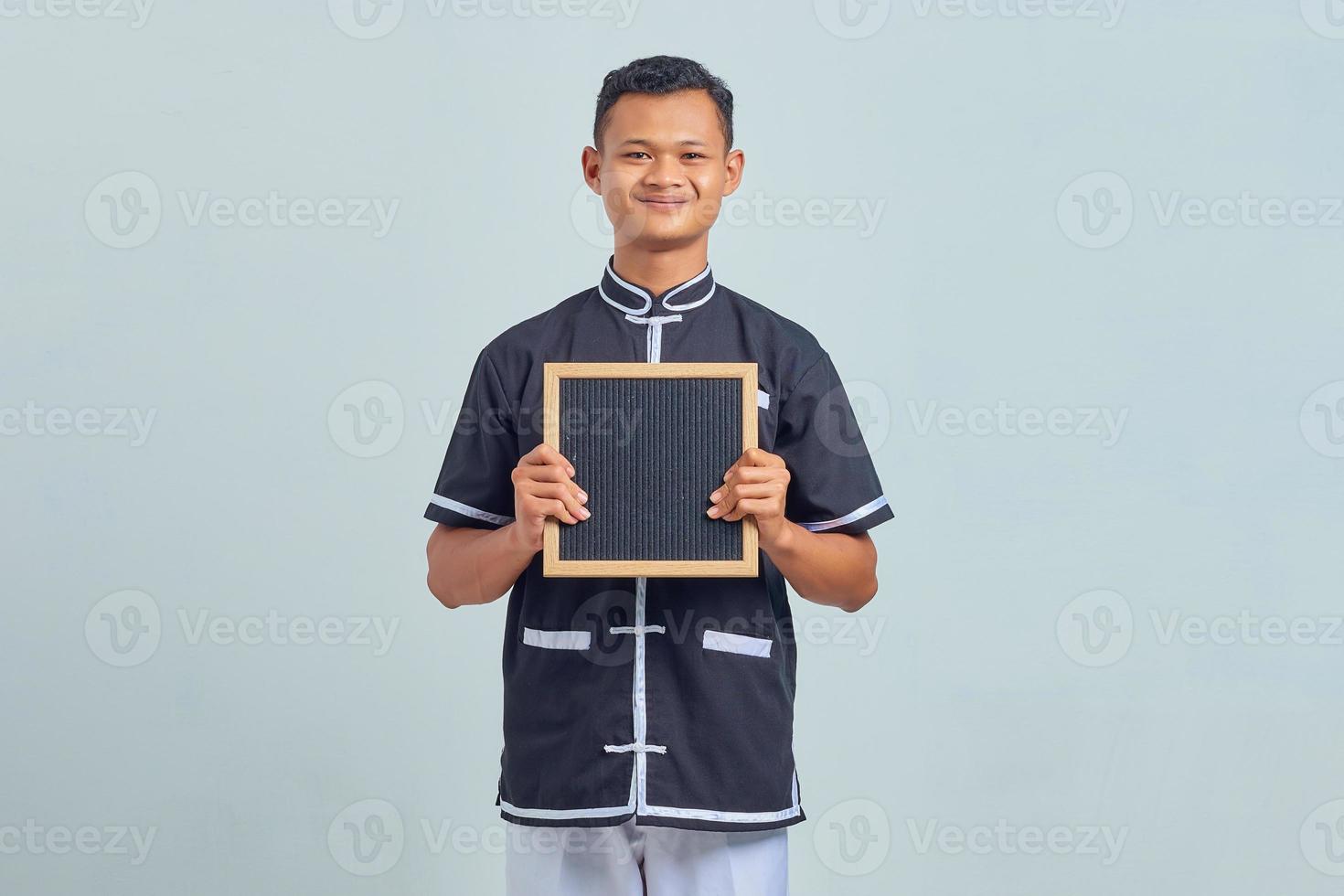 Portrait of excited Asian young man wearing karate uniform showing blank board on gray background photo