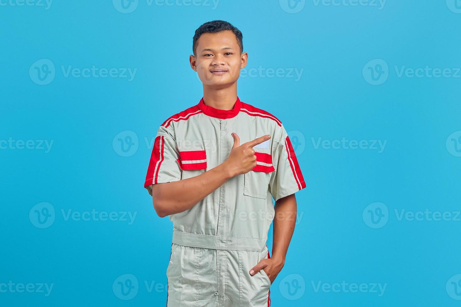 Portrait of smiling young mechanic pointing finger at copy space on blue background photo