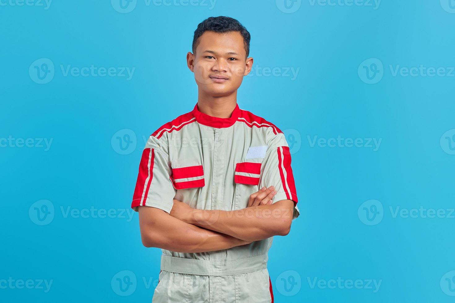 Angry young mechanic looking at camera and crossing arms isolated on blue background photo