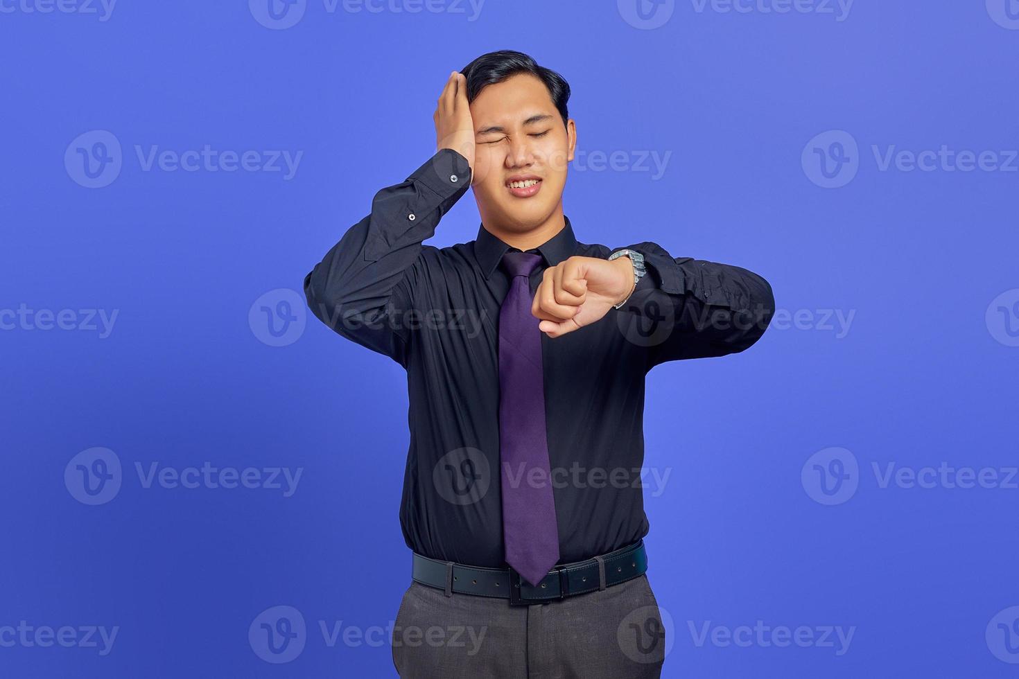 Smiling young handsome businessman checking time on wristwatch on purple background photo
