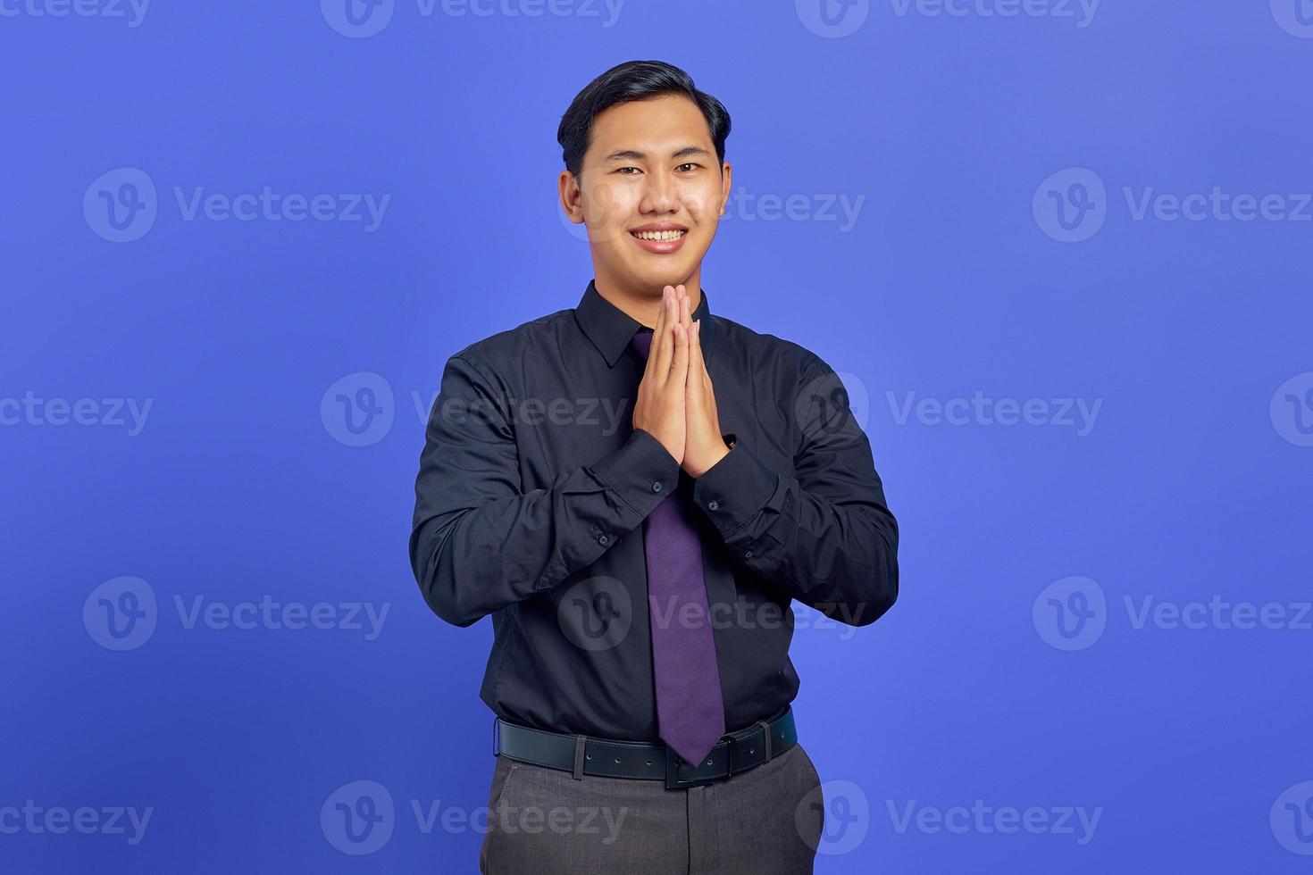 Smiling handsome young businessman with confident face giving hand greeting on purple background photo