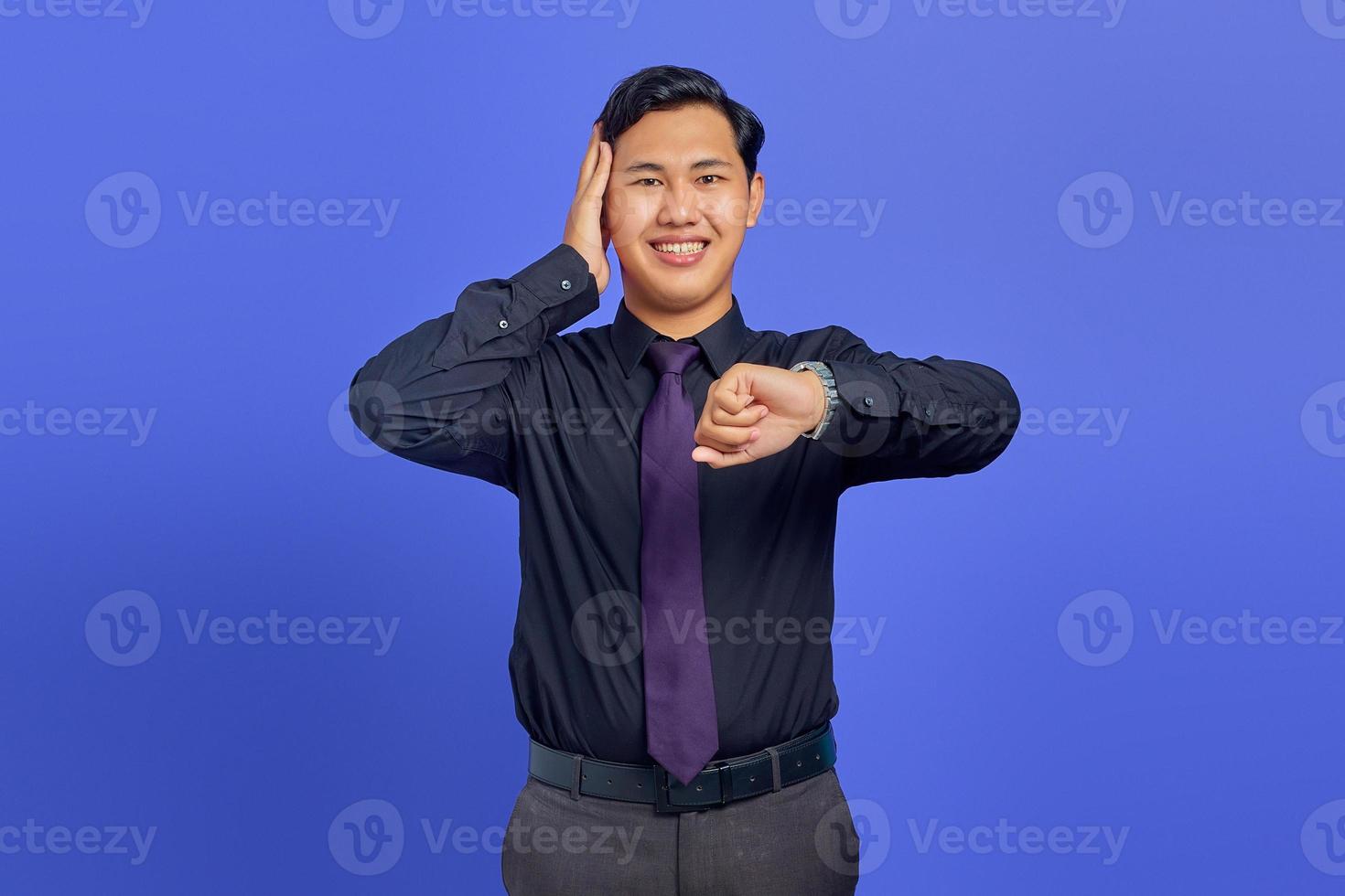 Smiling young handsome businessman checking time on wristwatch on purple background photo