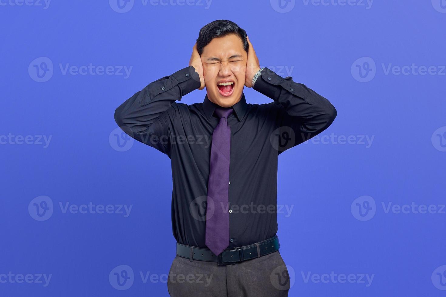 Frustrated young handsome businessman covering ear with anger expression on purple background photo