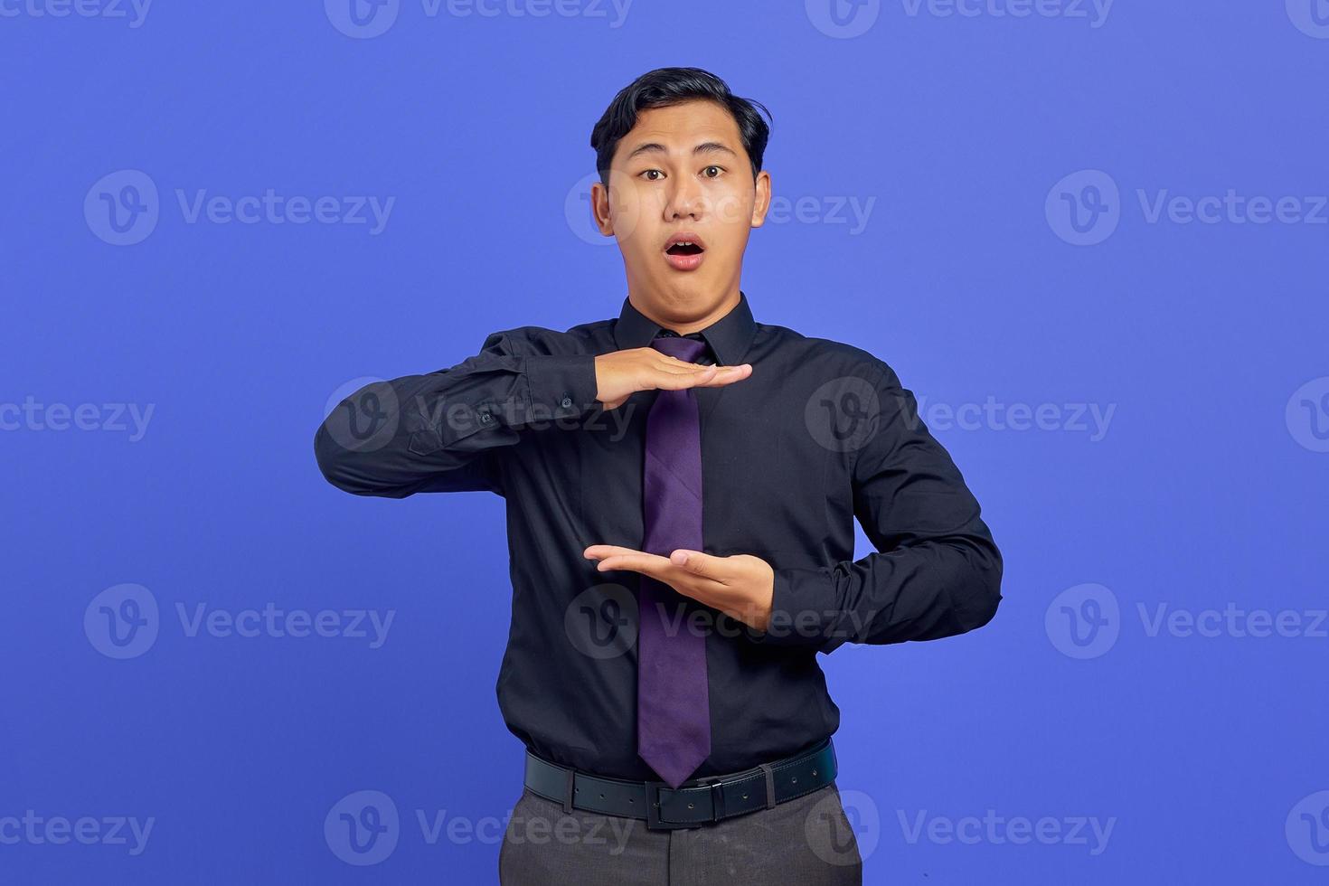 Portrait of surprised asian man showing product with palm over purple background photo