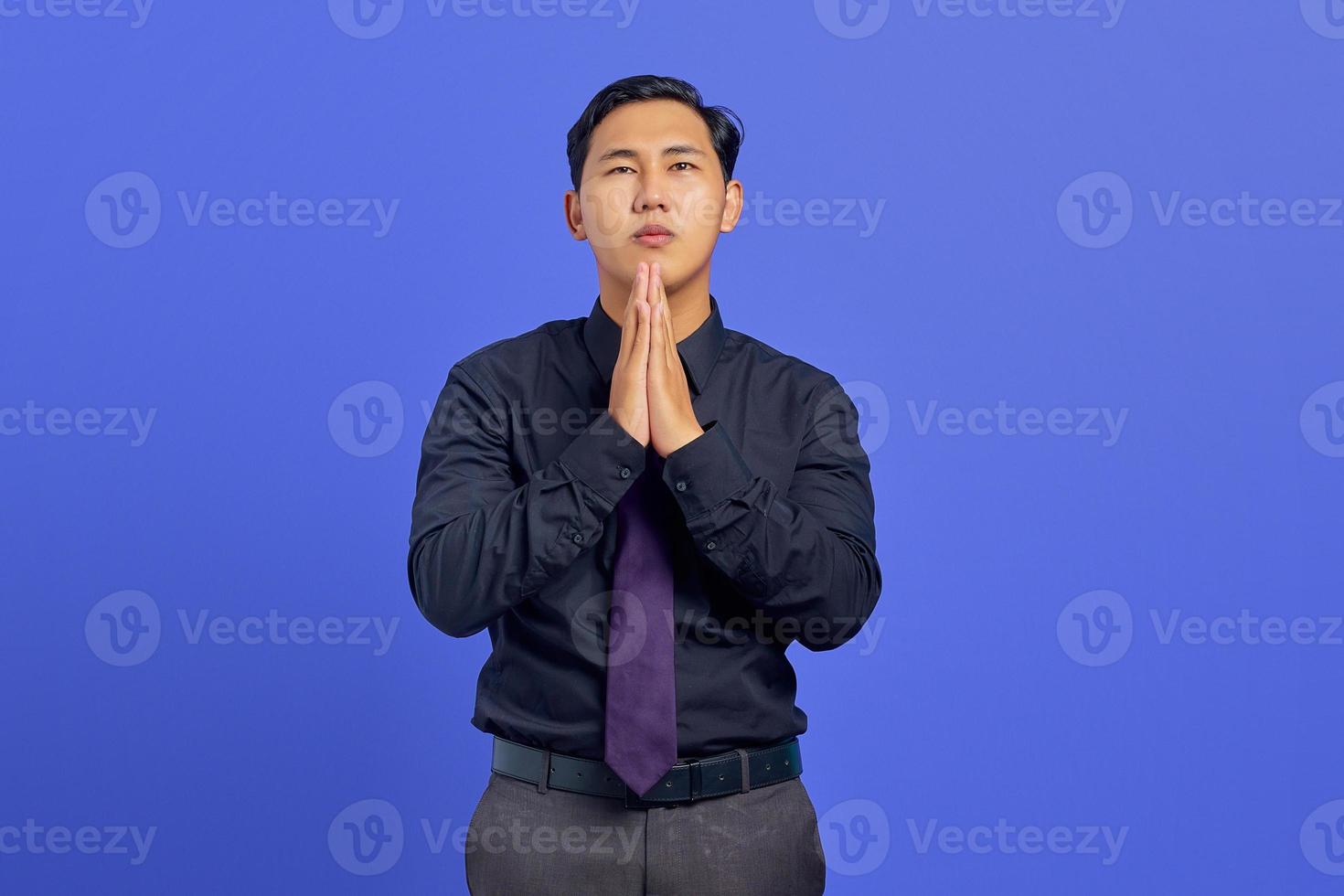 Retrato de tristeza joven asiático mostrando gesto de oración sobre fondo púrpura foto