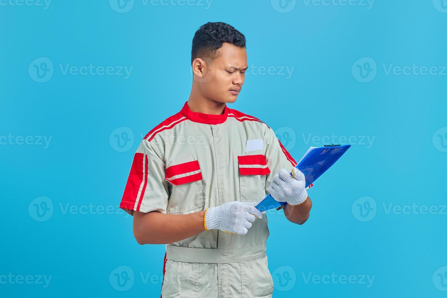 Shocked young Asian mechanic looking at notes on clipboard over blue background photo