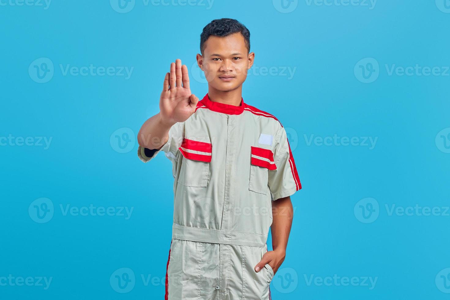 Portrait of young Asian mechanic doing stop motion with palm isolated on blue background photo