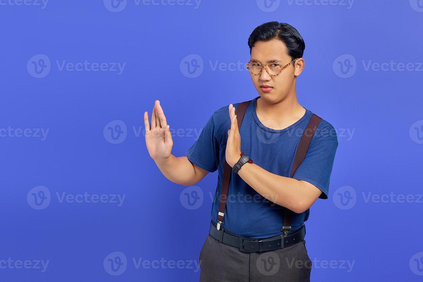 Portrait of nervous anxious young Asian man make stop don't move gesture over purple uebackground photo