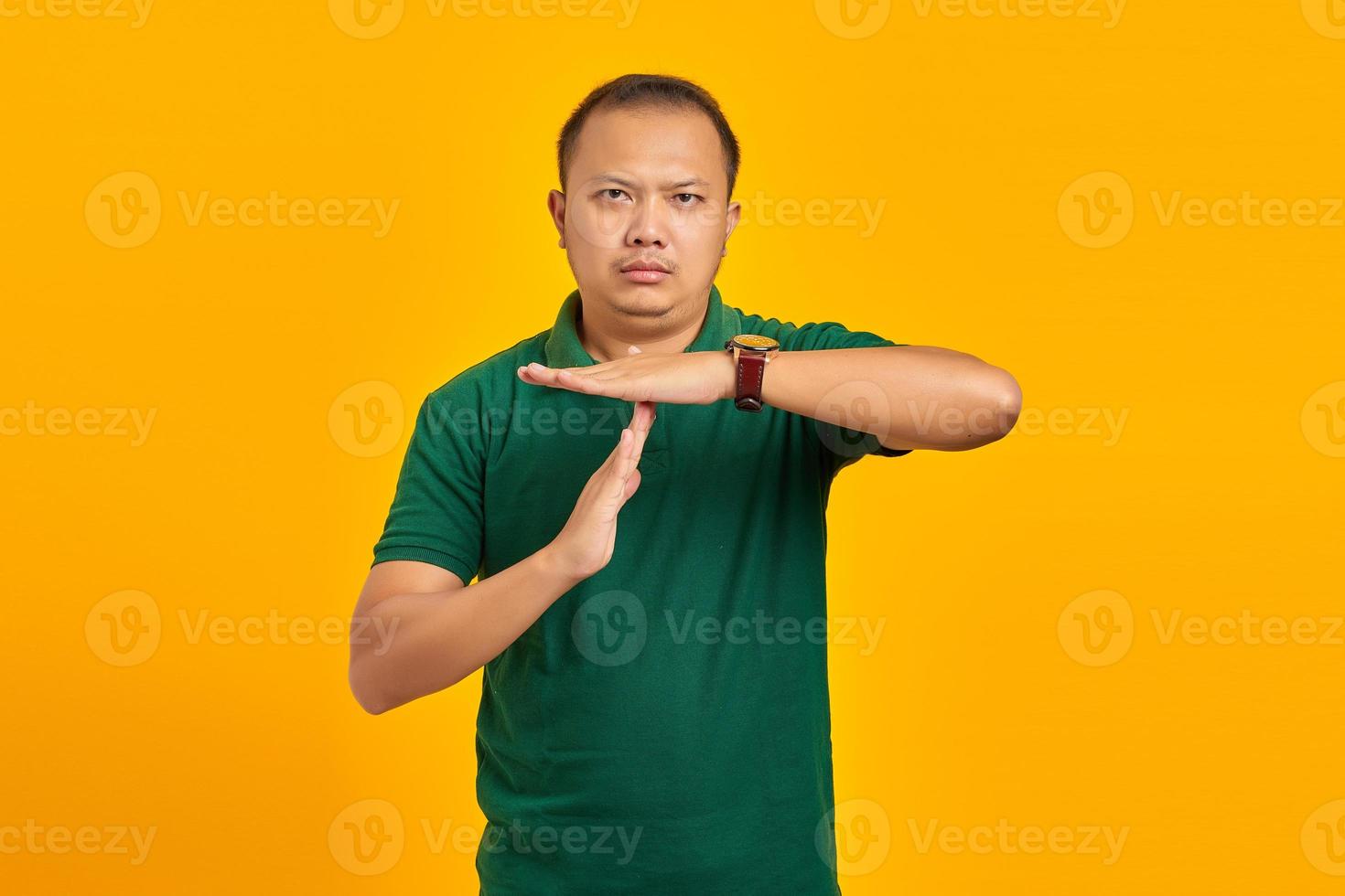 Portrait of handsome Asian man showing time limit gesture on yellow background photo