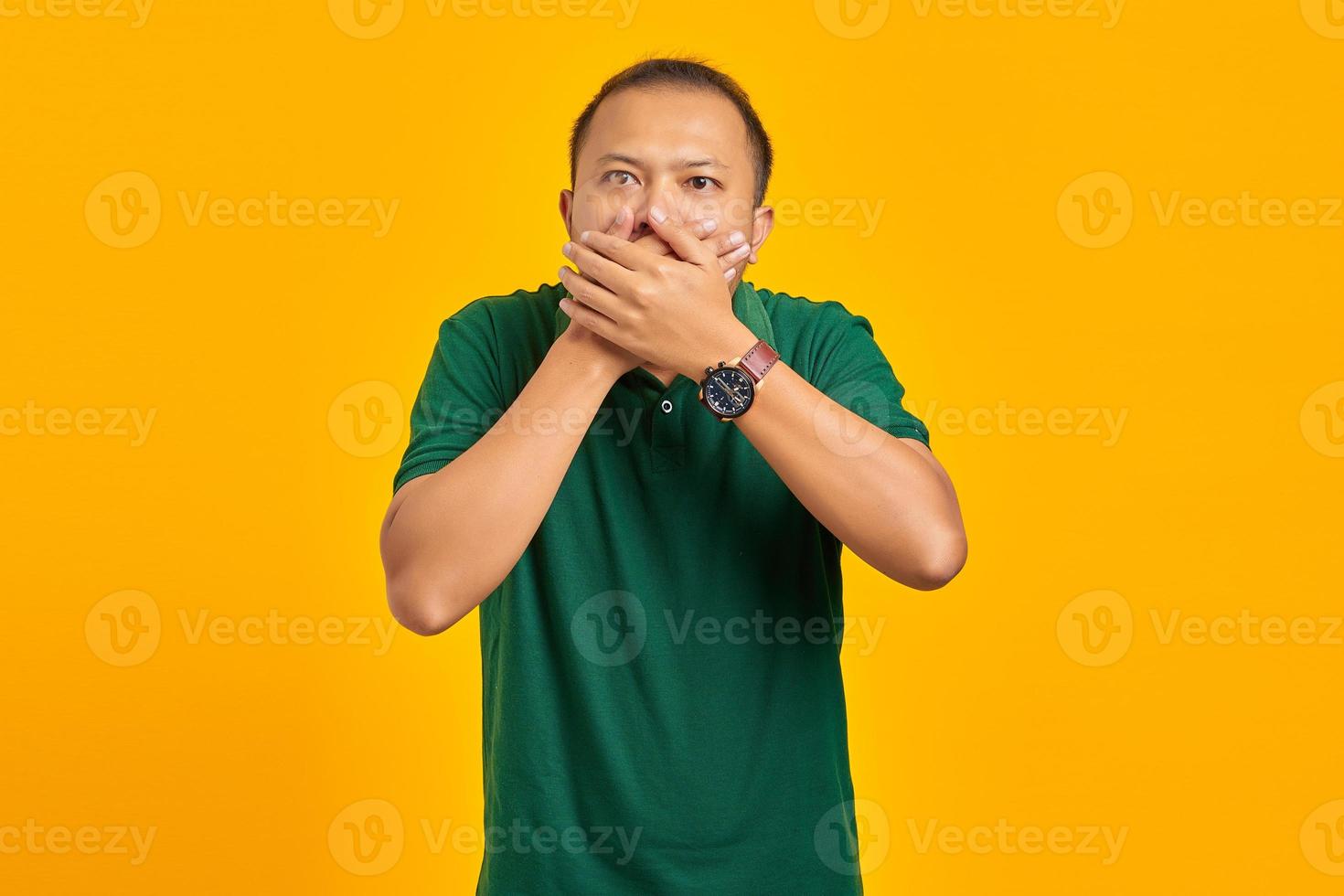 Surprised young Asian woman covering mouth with hand on yellow background photo