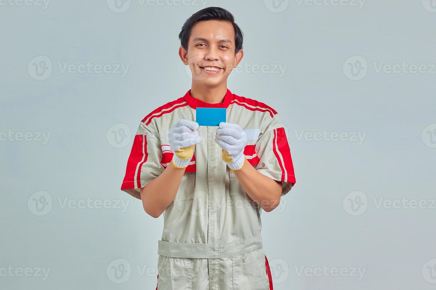 Portrait of handsome young mechanic showing credit card in hand on gray background photo