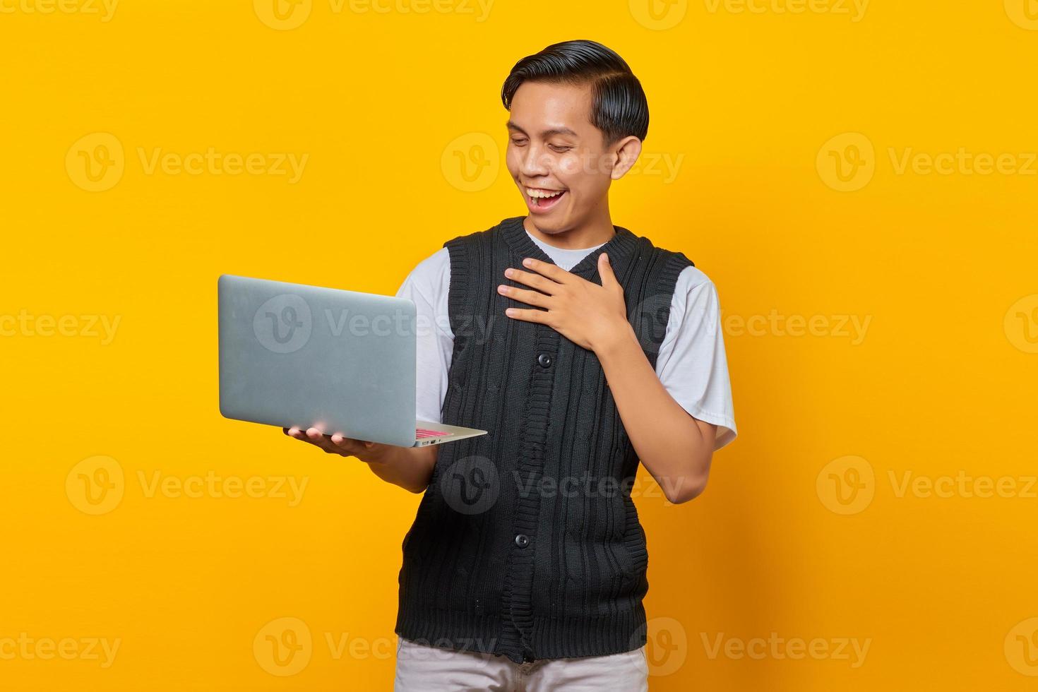 Portrait of excited Asian man holding laptop over yellow background photo