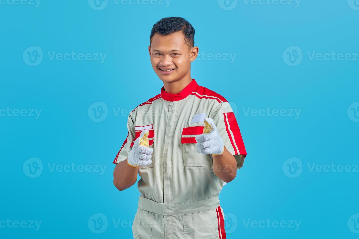 Smiling young asian mechanic pointing finger at camera isolated on blue background photo