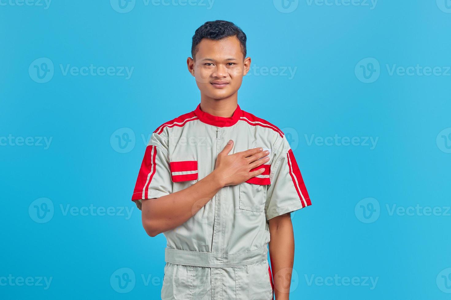 Retrato de sonriente joven mecánico asiático con palmas en el pecho sobre fondo azul. foto