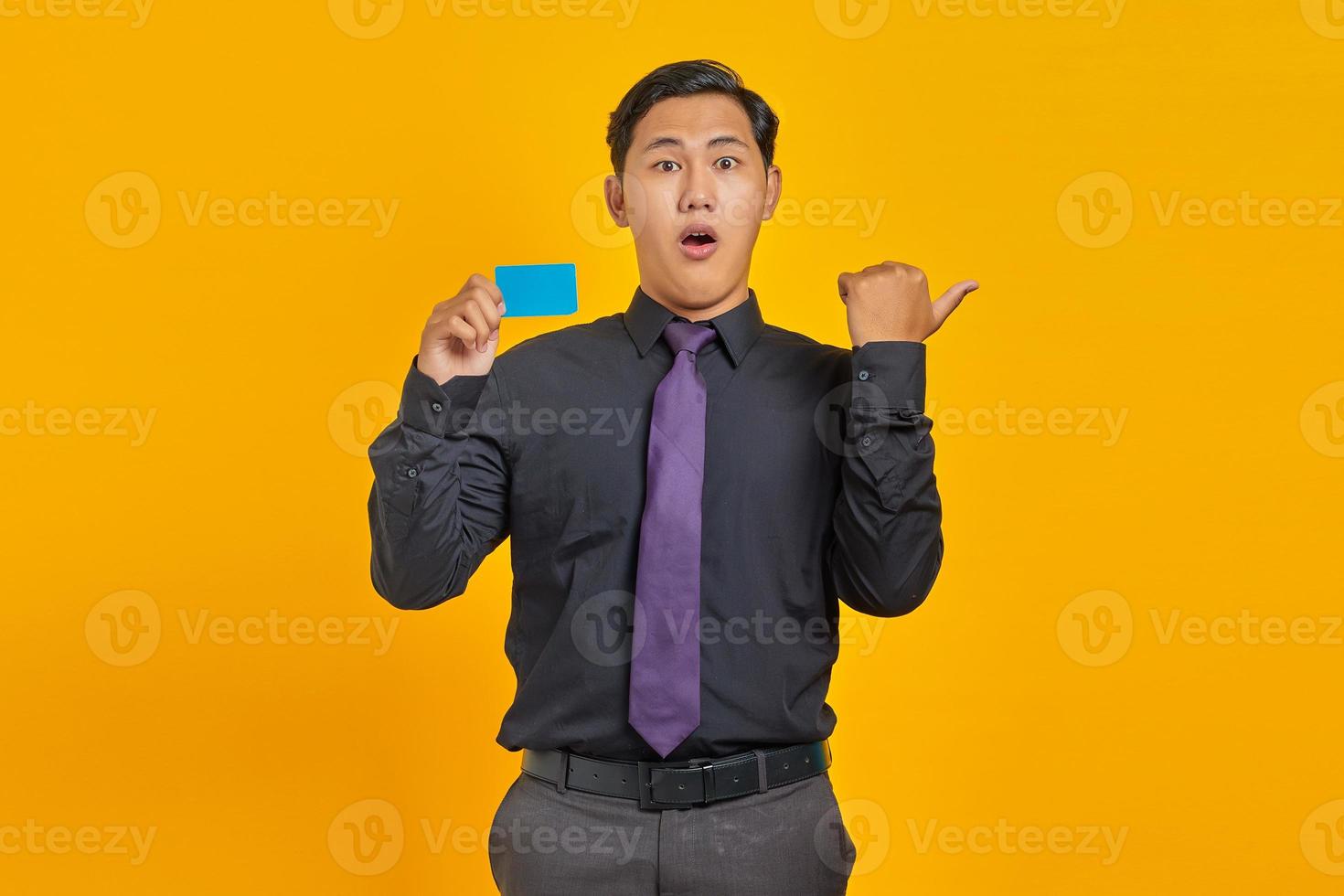 Shocked Asian businessman holding a credit card while pointing finger at copy space on yellow background photo