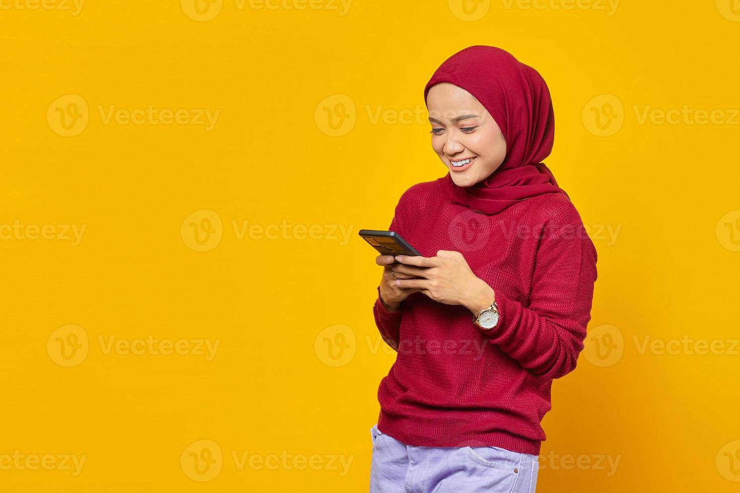 Happy young Asian woman using a mobile phone and looking smartphone screen on yellow background photo
