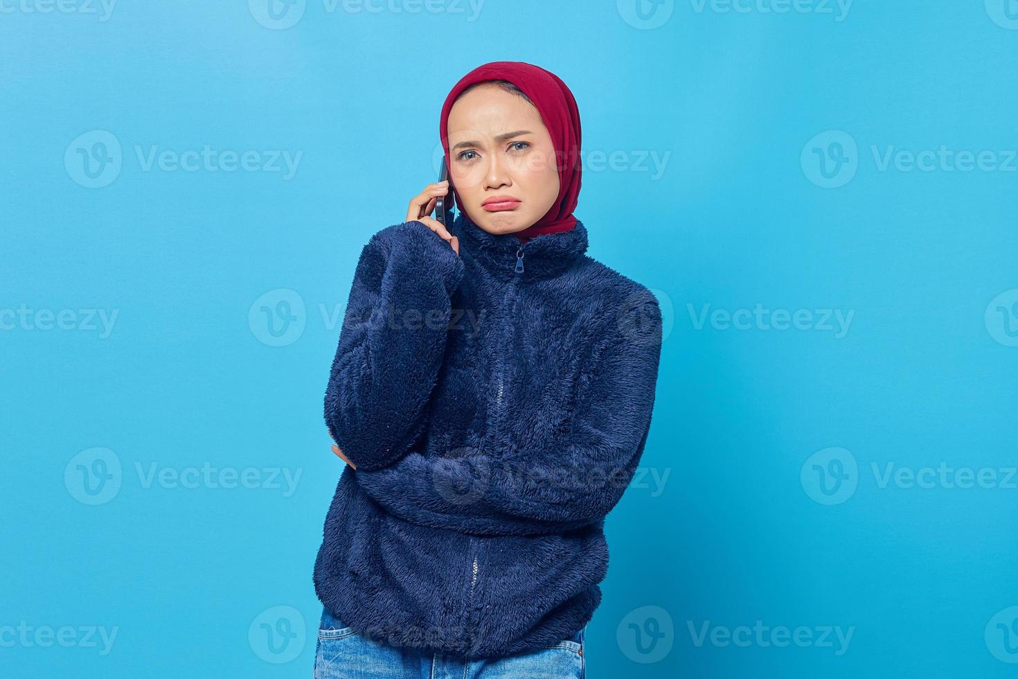 Triste joven asiática hablando por un teléfono móvil con su novio aislado sobre fondo azul. foto
