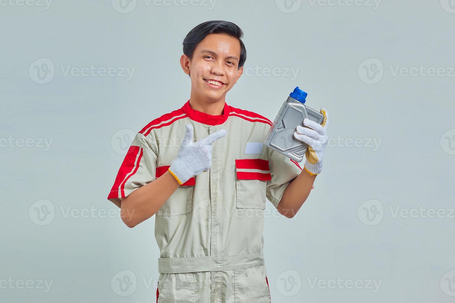 Retrato de hombre guapo sonriente vestido con uniforme de mecánico mostrando botella de plástico de aceite de motor sobre fondo gris foto