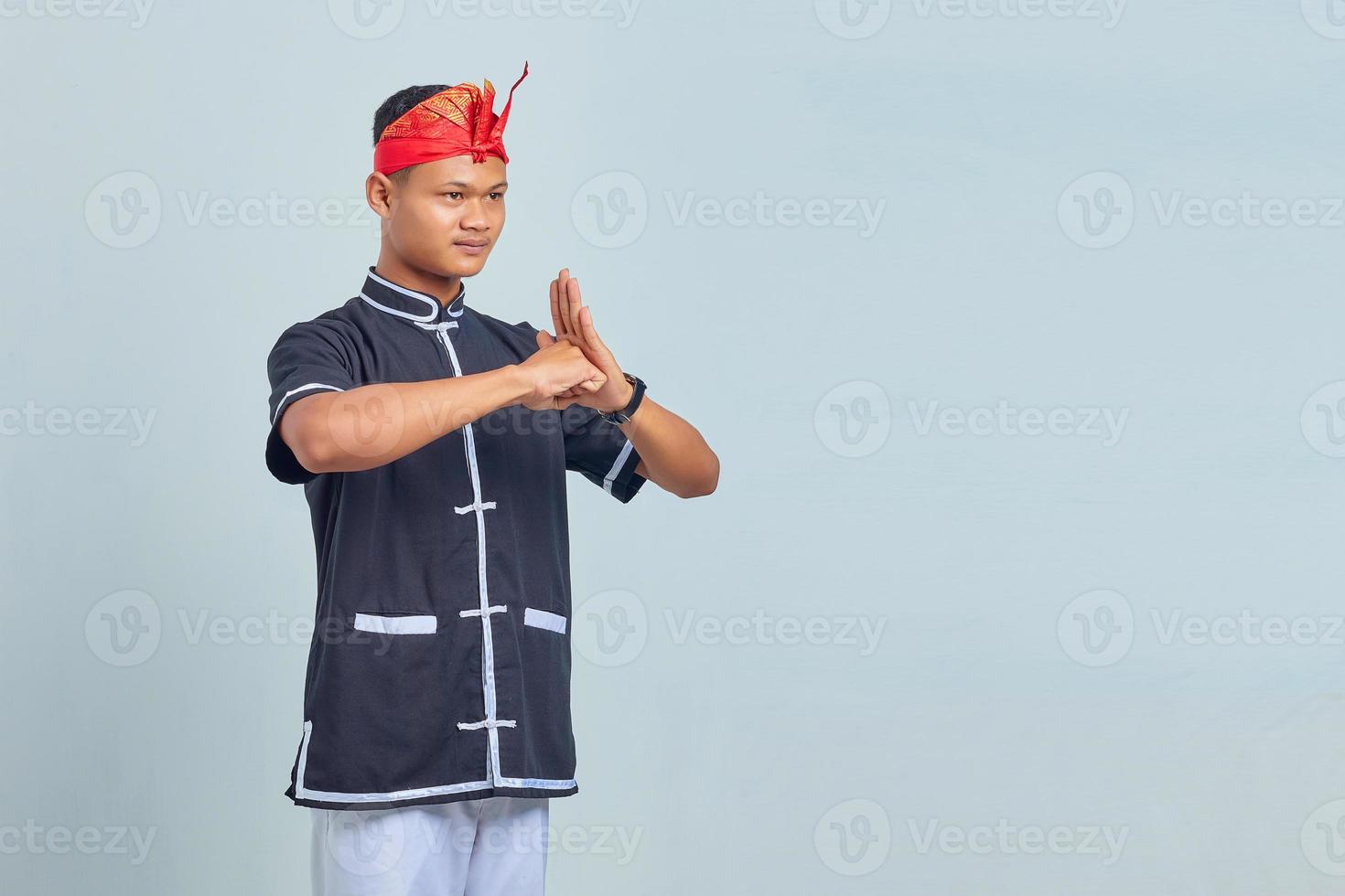 Portrait of Asian youth wearing taekwondo kimono with greeting gesture on gray background photo