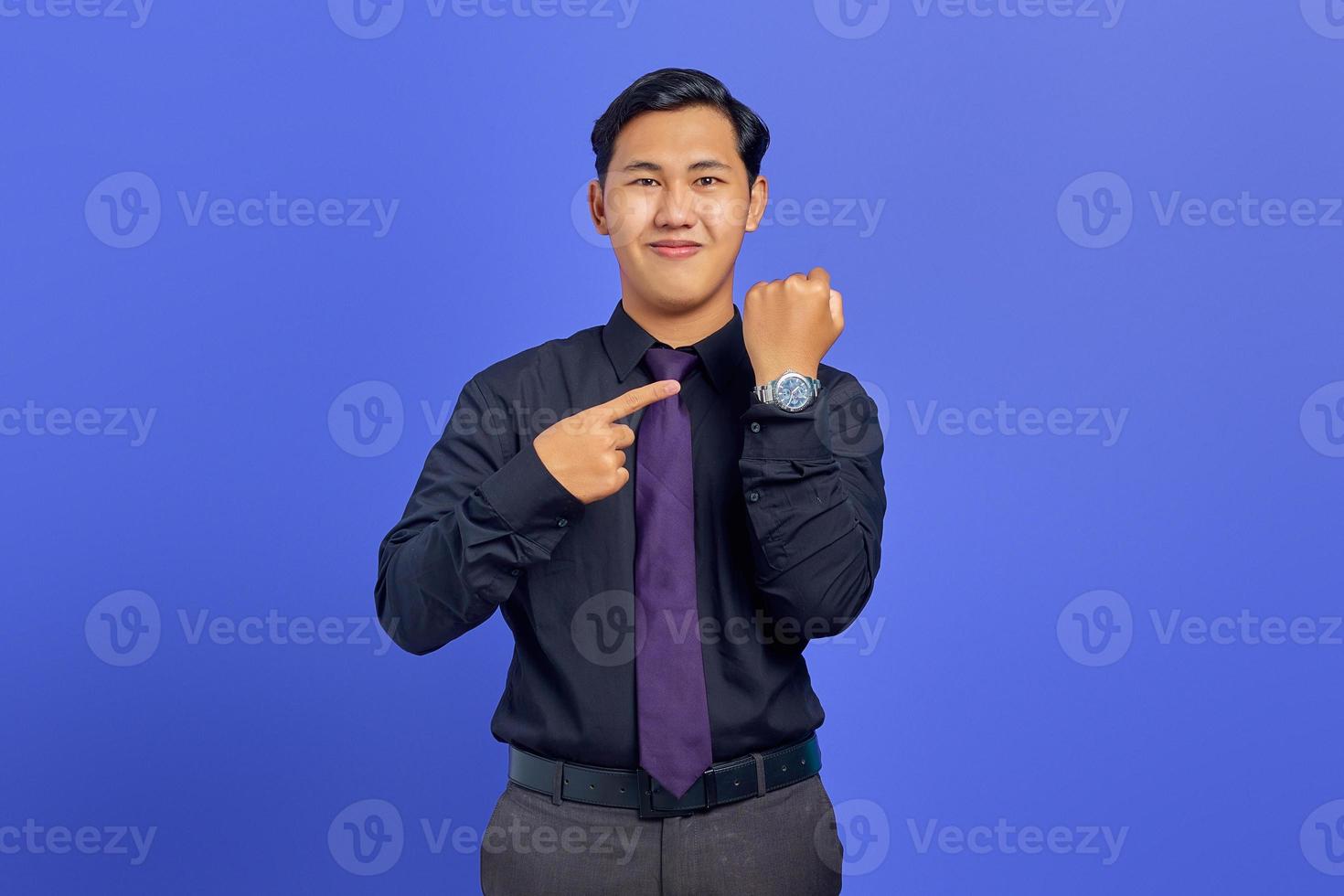 Smiling handsome young businessman checking time on wristwatch on purple background photo
