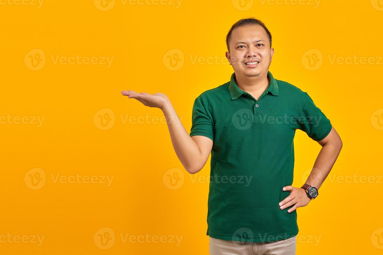 Smiling young handsome man showing copy space on palm on yellow background photo