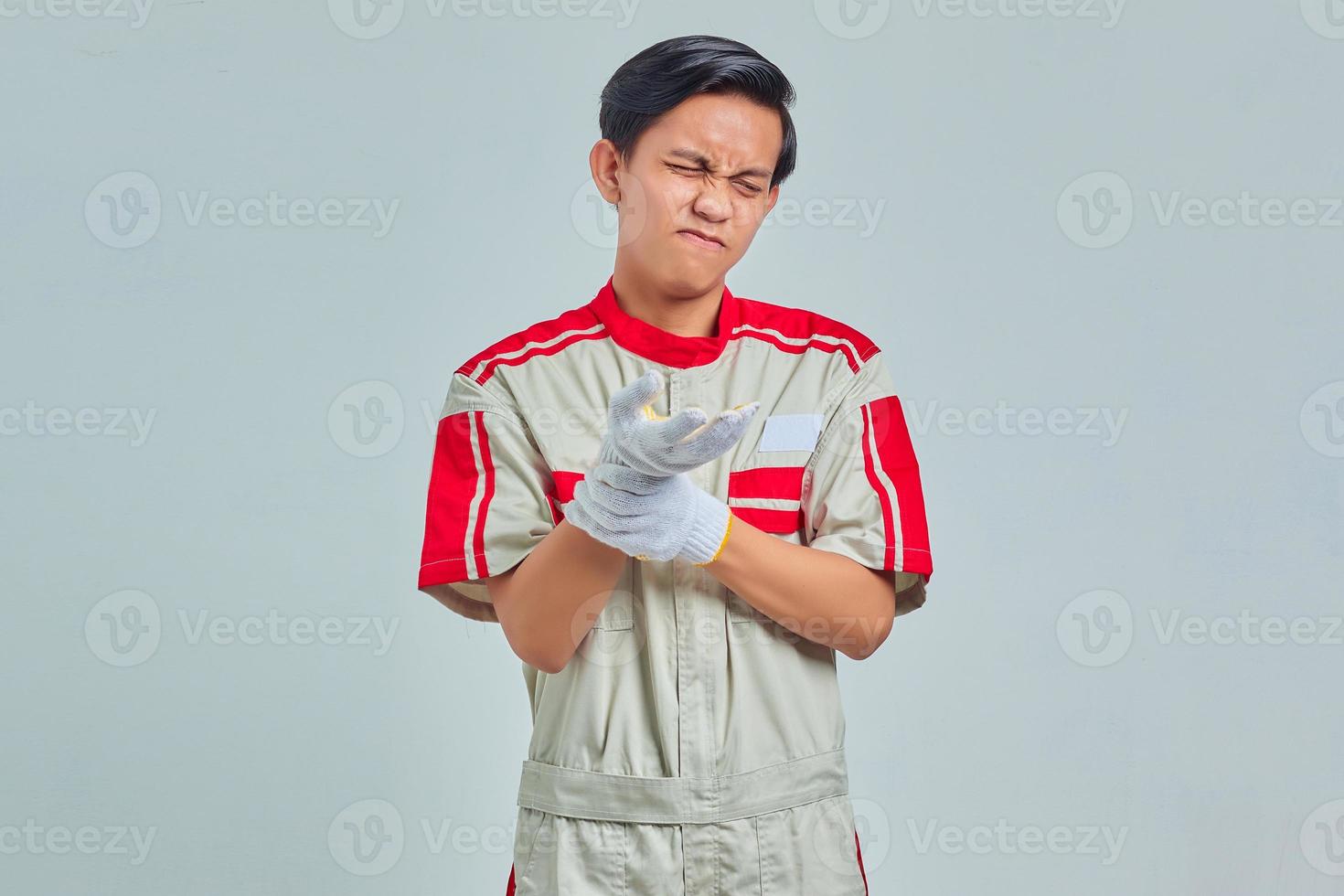 Portrait of handsome man wearing mechanical uniform suffering from pain in hands and fingers on gray background photo