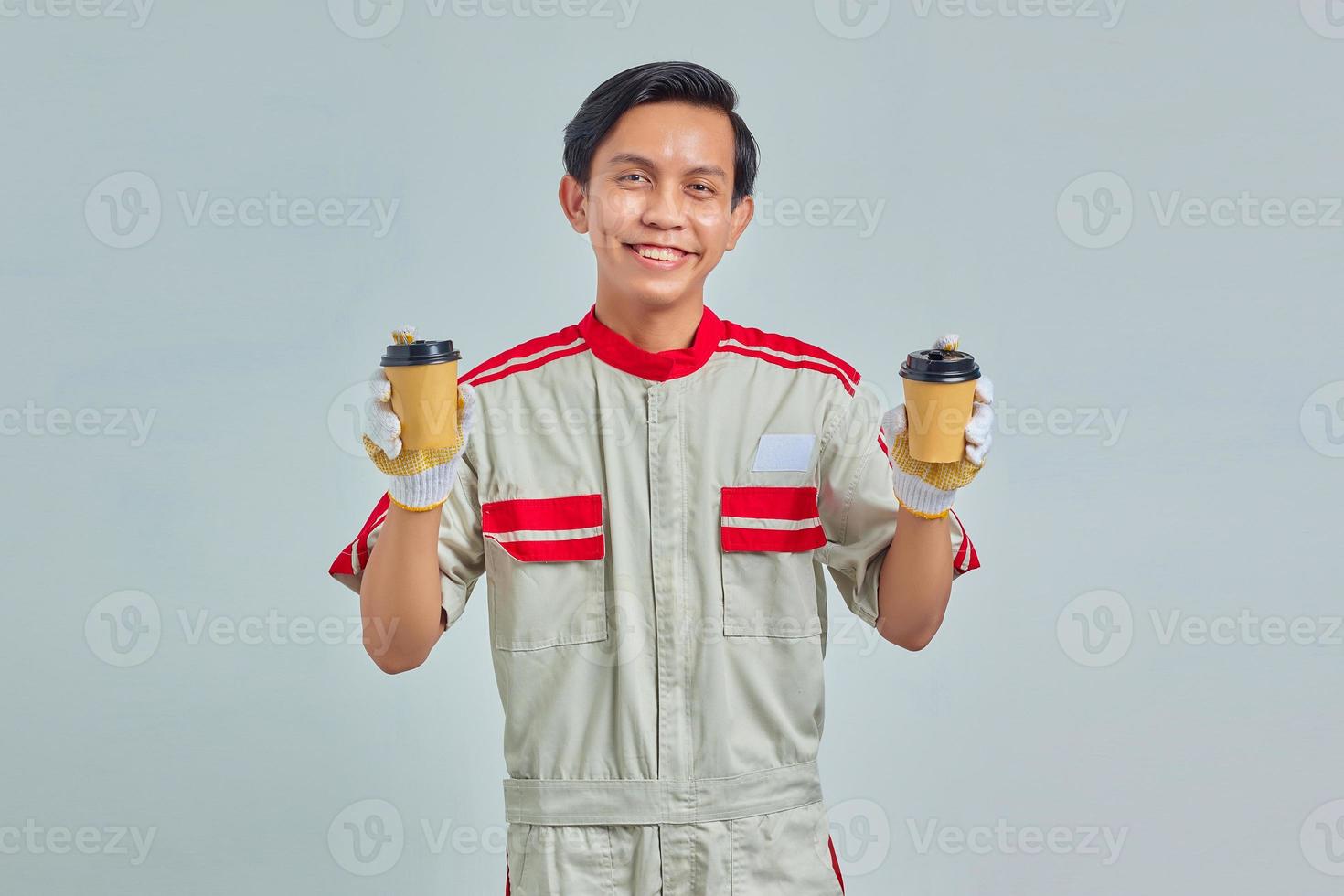 Smiling young mechanic holding showing coffee on gray background photo