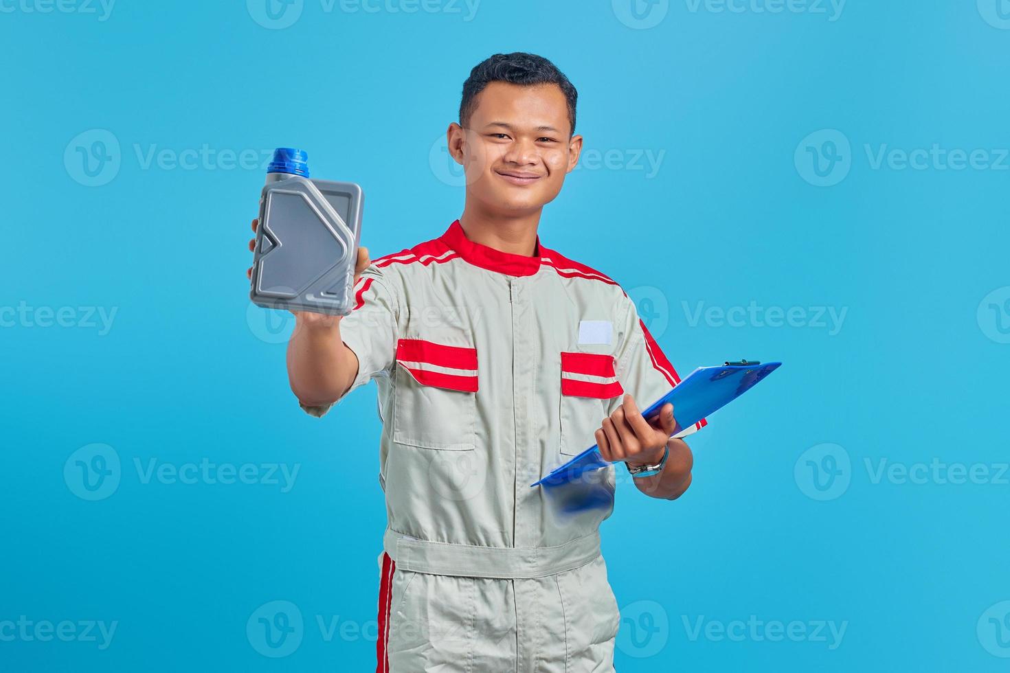Portrait of smilling young asian mechanic holding clipboard and showing plastic bottle of engine oil in hand over blue background photo