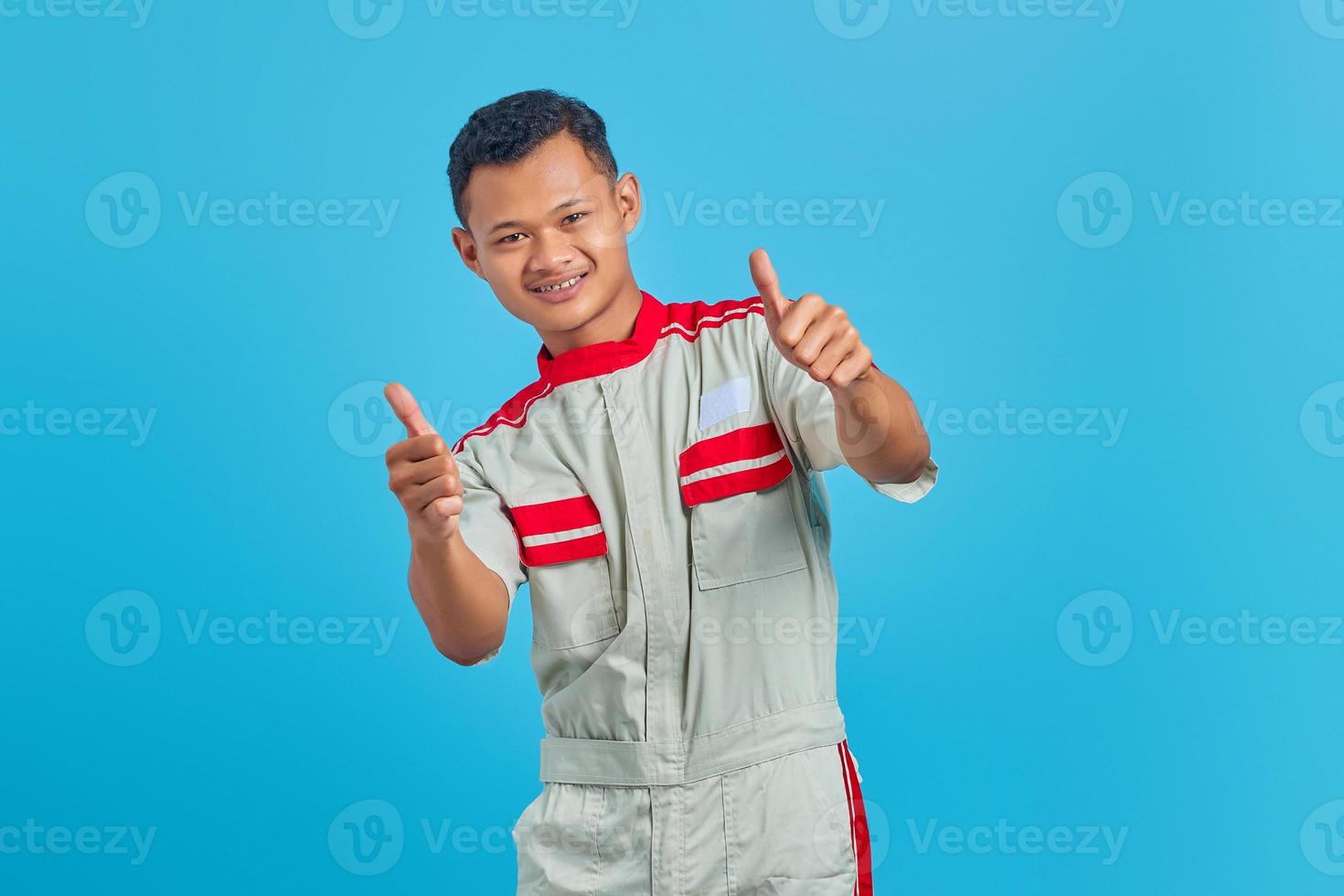 Portrait of excited young Asian mechanic showing thumb up gesture isolated on blue background photo