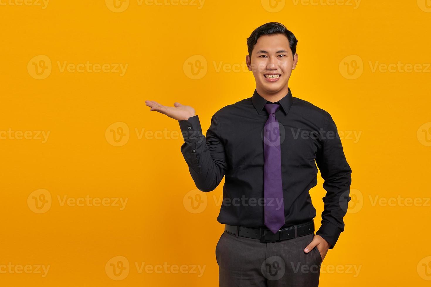 Smiling young handsome businessman showing copy space on palm on yellow background photo