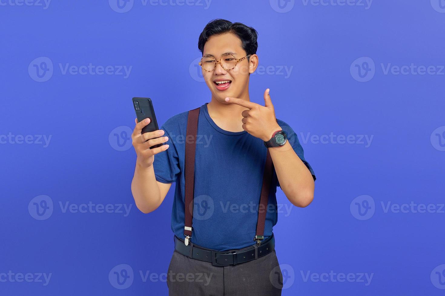 Portrait of smiling man pointing finger at cell phone on purple background photo