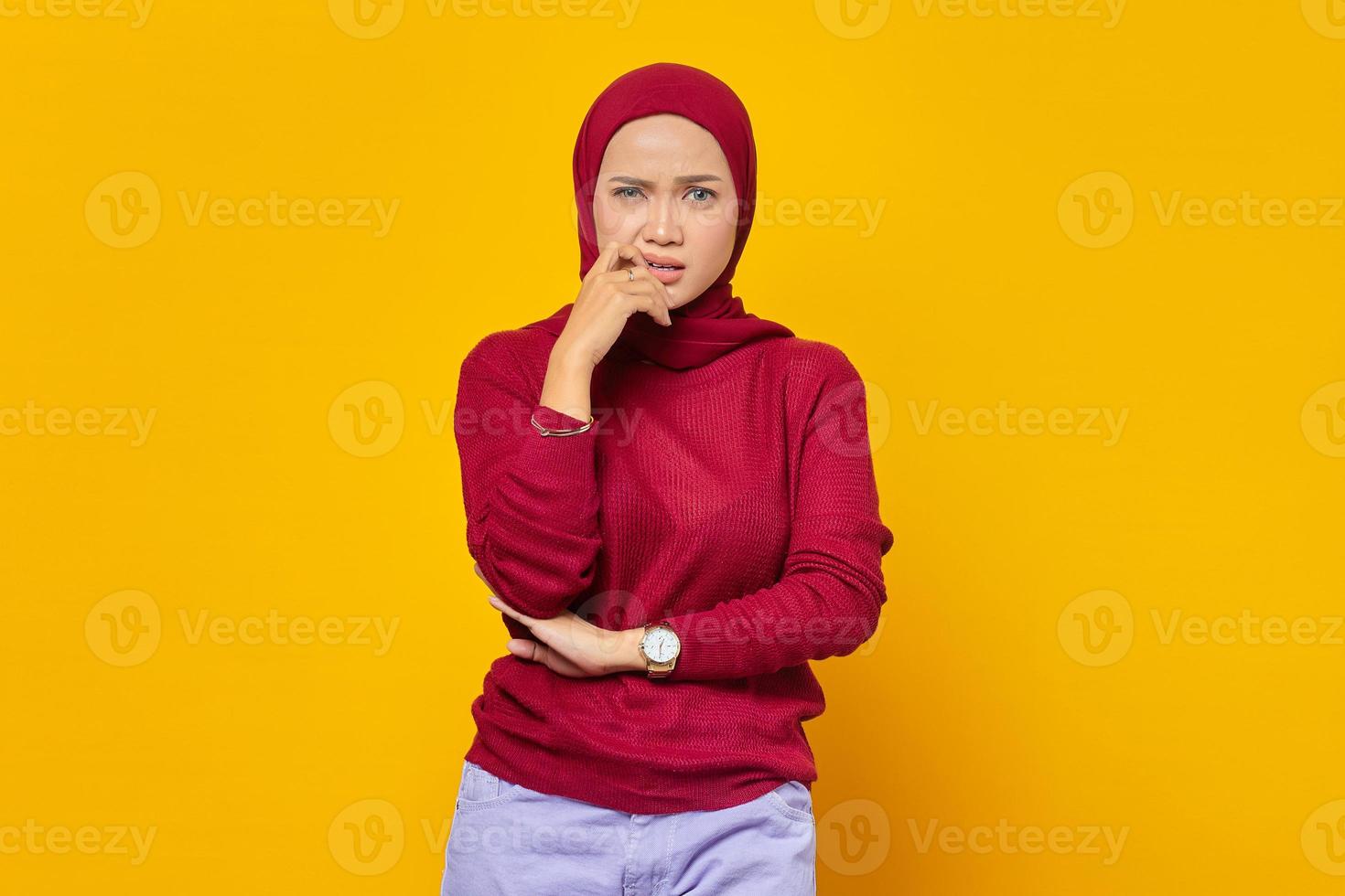 Retrato de mujer asiática joven de aspecto estresado y nervioso con las manos en la boca mordiendo las uñas aislado sobre fondo amarillo foto