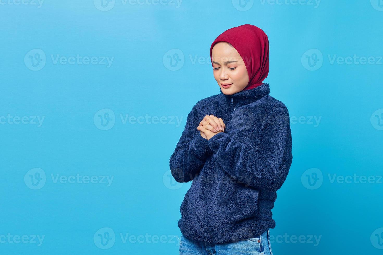 Atractiva joven asiática rezar y cerrar los ojos sobre fondo azul. foto