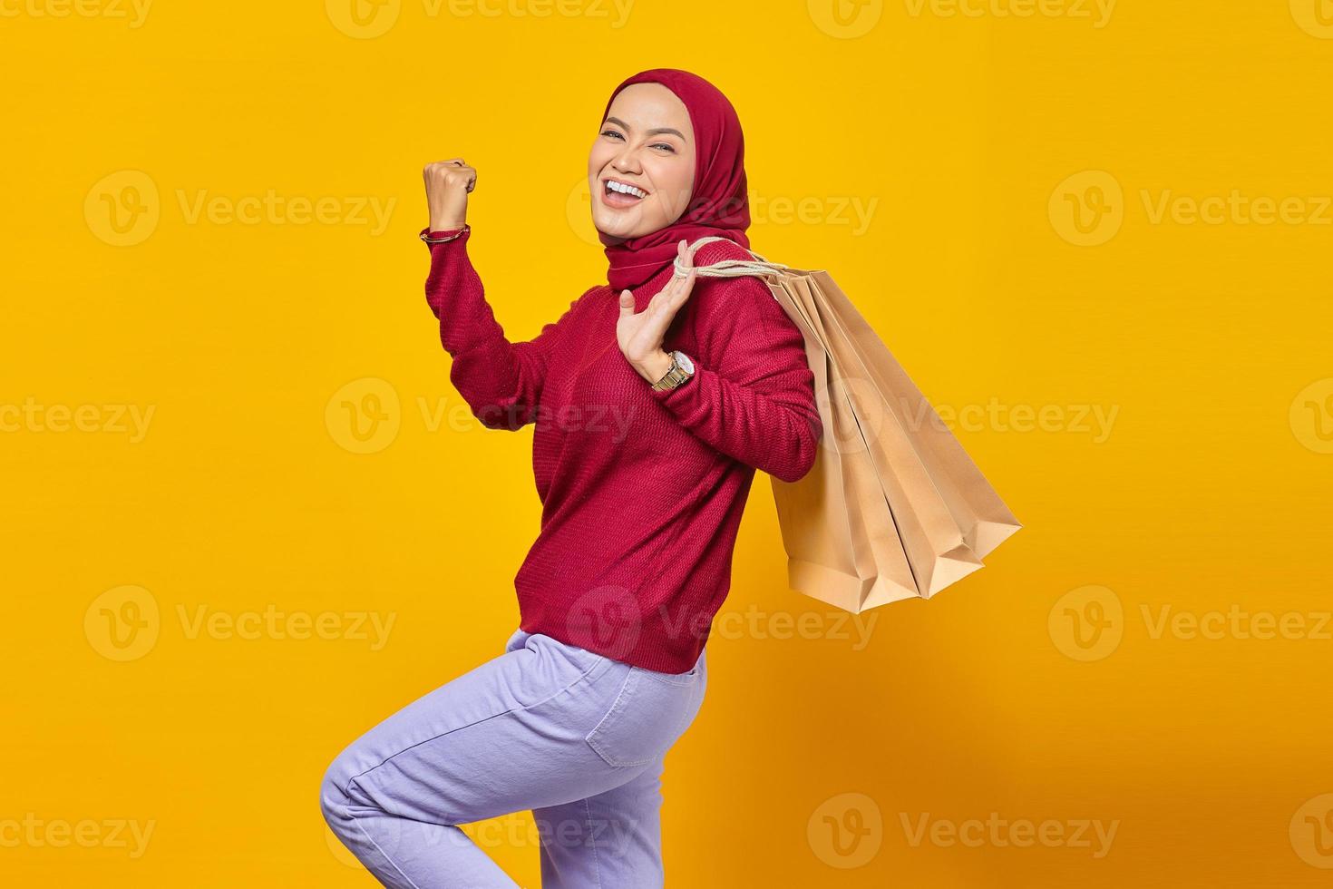 Emocionada y alegre joven asiática sosteniendo bolsas de la compra sobre fondo amarillo foto