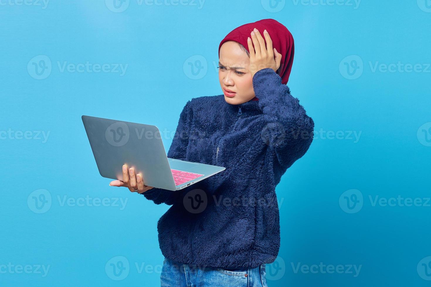 Hermosa mujer asiática usando laptop con expresión de sorpresa mirando y sosteniendo la cabeza con las palmas foto