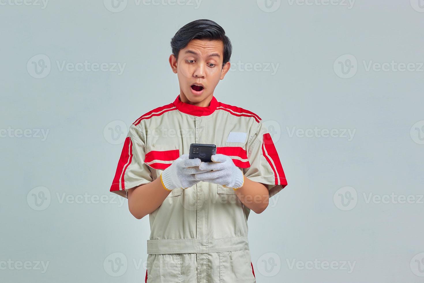 Surprised handsome man wearing mechanical uniform using cell phone isolated on gray background photo