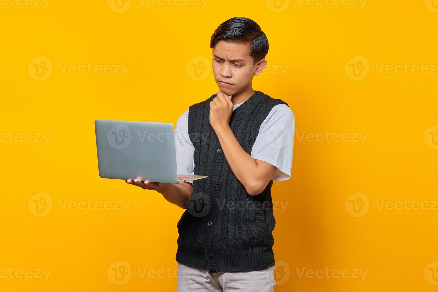 Portrait of confident Asian man holding laptop and looking at incoming email over yellow background photo