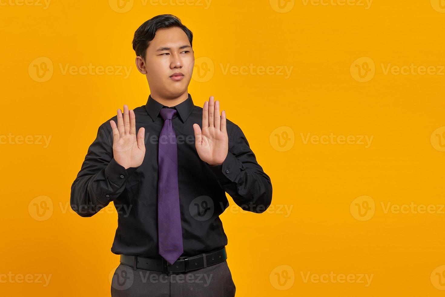 Portrait of angry young handsome businessman doing stop gesture with hand palms on yellow background photo