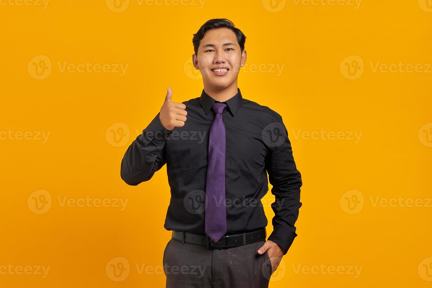 Alegre joven empresario asiático mostrando Thumbs up gesto aislado sobre fondo amarillo foto