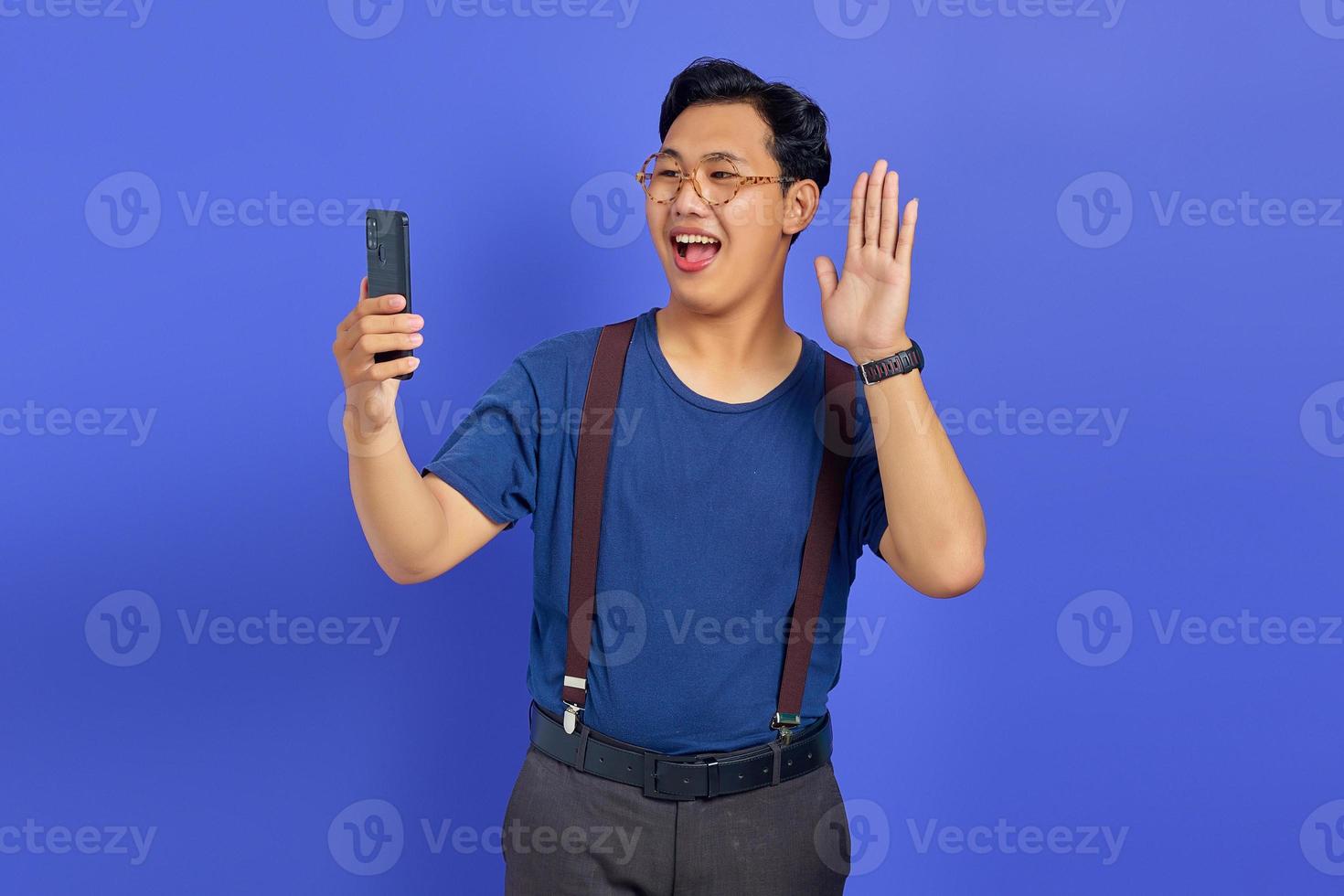 Retrato de feliz joven asiático a través de teléfono móvil con la mano saludando hacia el smartphone foto