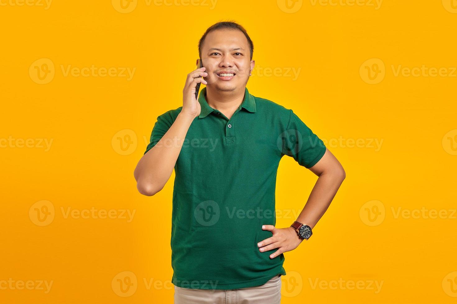 Retrato de sonriente joven asiático hablando por un teléfono móvil sobre fondo amarillo foto