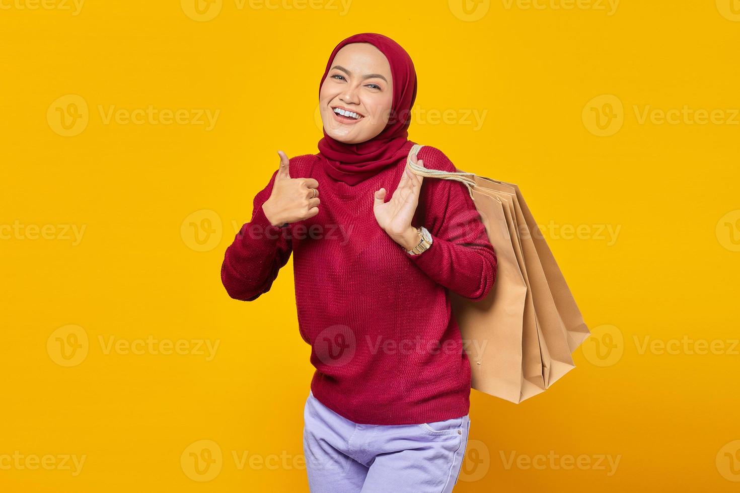Hermosa mujer asiática sosteniendo bolsas de la compra y mostrando los pulgares hacia arriba con cara sonriente foto