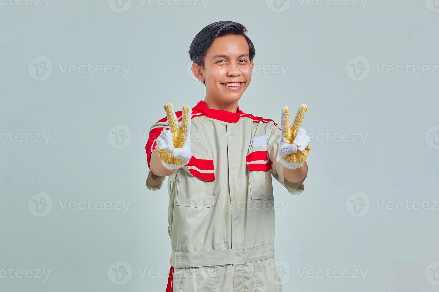 Portrait of cheerful handsome man wearing mechanic uniform making peace sign with fingers over gray background photo